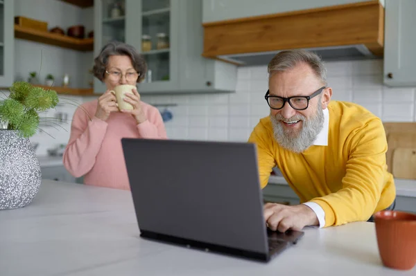 Elderly husband enjoying video game on laptop while old wife drinking coffee in need of attention. senior couple relationships and gadget addiction concept