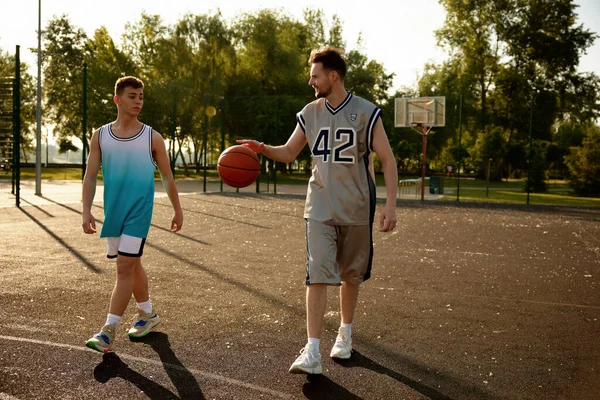 年轻的爸爸和十几岁的儿子在城市篮球场上散步 赛前或赛后交谈 — 图库照片