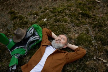 Rahatlamış yetişkin adam yürüyüşçüsü ormanda çimlere uzanıyor gökyüzünün güzel manzarasının tadını çıkarıyor kuşların şarkılarını dinliyor.