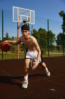 Sokak sahasında topla antrenman yapan aktif bir genç basketbolcu. Konsantre çocuk yaz günü şehir parkında oyun oynuyor.