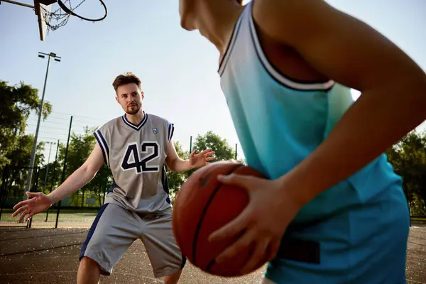 A teenager boy preparing to throw ball into basket hoop. Happy dad and son playing basketball on outdoor street court