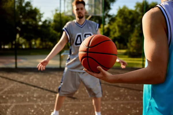 Street basketball concept, father playing on basketball with teenager son. Young trainer teaching boy passing ball. Focus on hand with game equipment