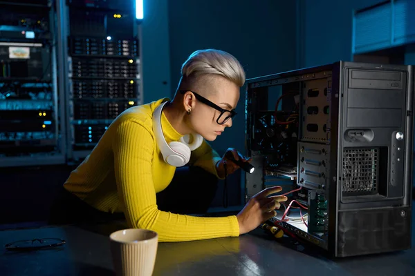 Young teenager hipster girl technician repairing computer part in datacenter. Female system administrator engaged in problem determination with cloud computing in server room