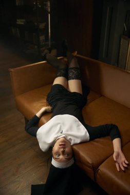 Gözleri kapalı, seksi iç çamaşırlarıyla kanepede yatan genç bir rahibe. Mükemmel vücutlu güzel bir kadın kamerada baştan çıkarıp flört ediyor.