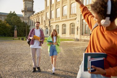 Çok ırklı bir grup öğrenci tatilde üniversite kampüsünde buluşuyor. Dışarıda dikilen, gündelik kıyafetler giyen mutlu, ırklar arası genç sınıf arkadaşları.