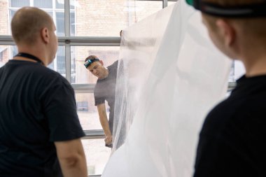 Araç servisi ekibi zırhlı ppf filmini yüklemeye hazırlanıyor. Otomobil tamirhanesinde çakıl önleyici kaplama.