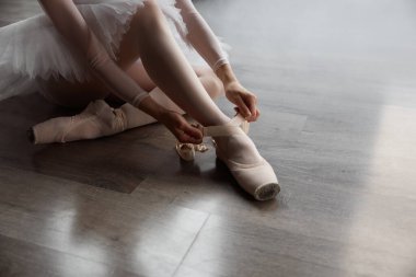 Balerin yerde oturuyor ve koreografi dersinden önce sivri uçlu ayakkabılar giyiyor. Dans okulundaki performans veya eğitime hazırlanan güzel bayan dansçı.