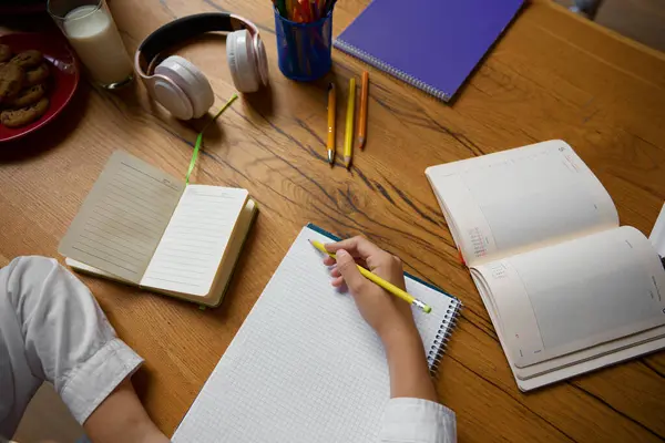 コピーブックに手書きの小さな学生の手の高角度ビュークローズアップ 自宅で宿題を学ぶ小学生 — ストック写真