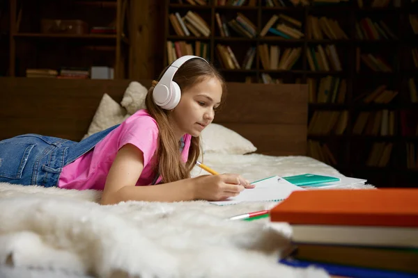 Cute little girl studying at home with wireless headphones. Adorable kid student having web lesson enjoying distance learning