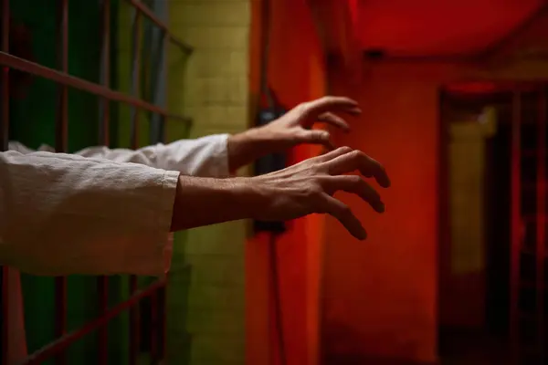 Closeup focus on creepy reaching hands with curled fingers of psychiatric clinic patient from cage ward