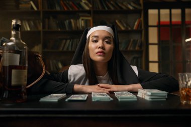 Genç ve gururlu bir kadının portresi rahibe cübbesi giymiş masaya oturmuş para içinde yüzüyordu.