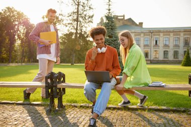 Üniversite kampüsündeki mutlu öğrenciler ödevlerini yapmak için dizüstü bilgisayar kullanıyorlar. Sınıf arkadaşları sosyal ağda komik videolar izliyorlar ya da mola sırasında araştırma yapıyorlar