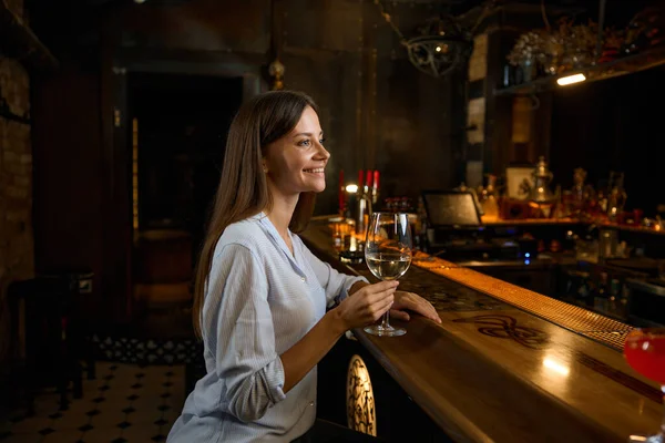 Happy smiling woman celebrating personal achievement resting at bar counter. Young female drinking wine chilling at restaurant