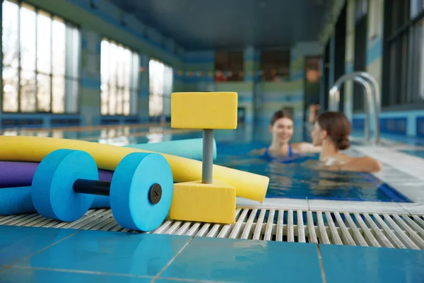 Aqua aerobics class, gymnastics training lesson at health club with swimming pool. Selective focus closeup on fitness sport equipment and instructor talking with client on blurred backdrop