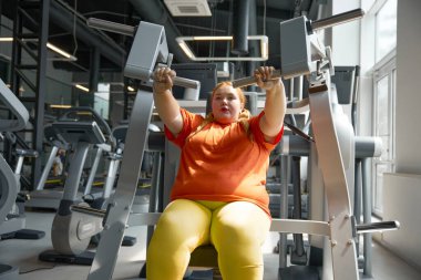 Güzel, genç, tombul bir kadın spor aletleriyle çalışıyor. Kendine güvenen obez kadın kilo vermek için egzersiz yapıyor.