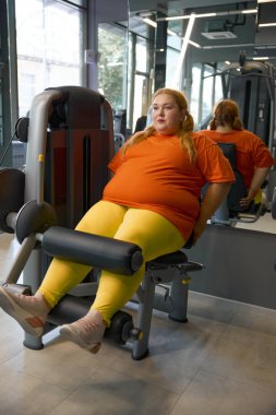Güzel tombul kız spor kıyafeti eğitimi spor aletleri üzerinde bacak pompalama egzersizi yapıyor.