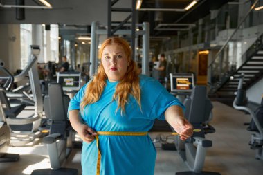 Tatmin olmuş kilolu bir kadın spor salonundaki zayıflama antrenmanından sonra ilk iyi sonucu ölçüyor.