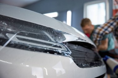 Araç temizleme servisinde arabanın üstünü koruyucu filmle örten teknisyen. Otomobil farına yakın görünüm seçici odak