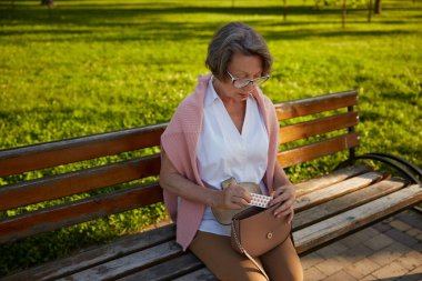 Yaşlı kadın parkta yürürken kötü hissettikten sonra çantasından haplar alıyor. Yaşlıların sağlık sorunları kavramı