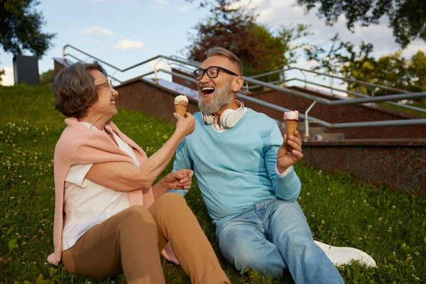 Happy joyful senior couple eating ice-cream in park. Elderly married man and woman fooling around making jokes having snack during walk