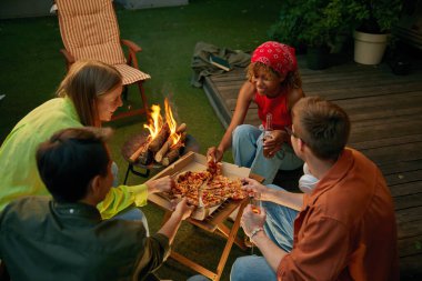 Mutlu arkadaşlar pizza ve biranın keyfini çıkarıyorlar. Yanan kamp ateşinin yanında içiyorlar. Çeşitli gençler güzel sohbetler yapıyorlar. Kamp yaparken mutlu bir ifade takınıyorlar.