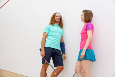 Spor giyinmiş genç bir adam ve kadın iç saha antrenman kulübünde squash maçından önce konuşuyorlar.