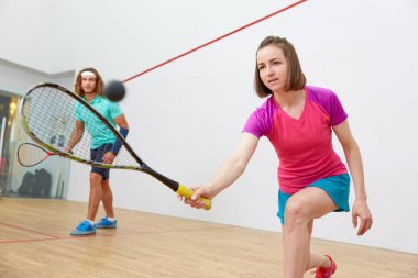 Genç ve sportif bir çift kapalı alanda squash oynuyor. Çekici bir kadının raketle topa vurmasına odaklan