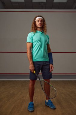 Kendine güvenen erkek squash oyuncusunun portresi raketle kameraya güvenle bakmaya hazır.