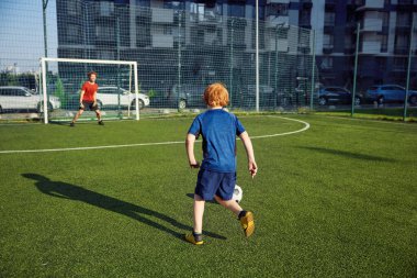 Baba ve oğlu güneşli yaz gününde sahada futbol oynuyorlar. Aile hafta sonu spor aktiviteleri