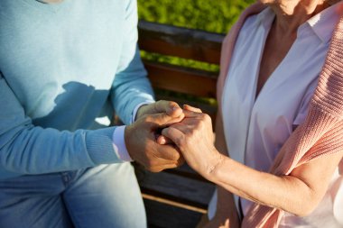 Son sınıf çifti el ele tutuşurken yakın çekim görüntüsü. Yaşlı adam ve kadın birbirlerine sevgi, destek ve empati gösteriyorlar. Halk parkında yaşlı insanlar için romantik bir randevu ve yürüyüş.