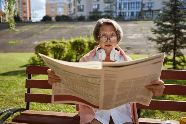 Surprised or shocked elderly woman reading daily newspaper finding overwhelmed news in morning in public park