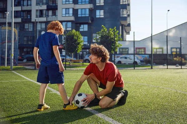 父親は息子にシティスタジアムでサッカーをするように教えています パパは サッカーボールをキックする方法を少年に話す スポーティブな家族のレクリエーション ストックフォト