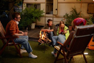 Gitar çalan bir grup arkadaş doğada kamp ateşinin yanında müzik dinliyorlar. Tatil ve açık hava seyahati kavramı