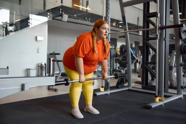 Kilo vermek ve güç pompalamak için halterli genç, şişman kadın antrenmanı. Spor salonunda kişisel spor eğitimi.