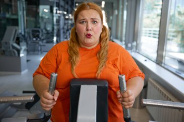 Eliptik makine üzerinde çalışan yorgun, terli obez kadının portresi. Spor salonunda yoğun kardiyo çalışması.