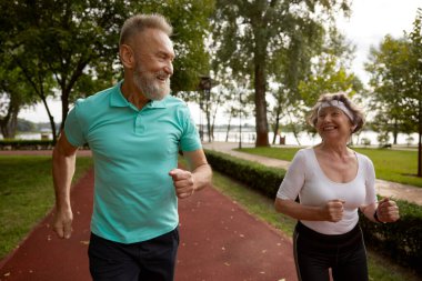 Son sınıf çifti doğa parkında birlikte koşuyor. Mutlu sağlıklı yaşlı kadın ve olgun erkek arkadaşlar dışarıda egzersiz yapıyor.