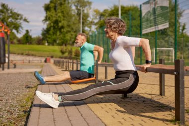 Mutlu sportif yaşlı çift oyun alanında antrenman yapıyor. Vücut geliştirme ve yaşlıların refahı için sabah antrenmanı.