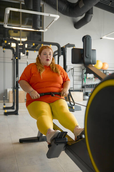 Chubby woman working hard on training machine at gym. Obesity struggle and sports concept