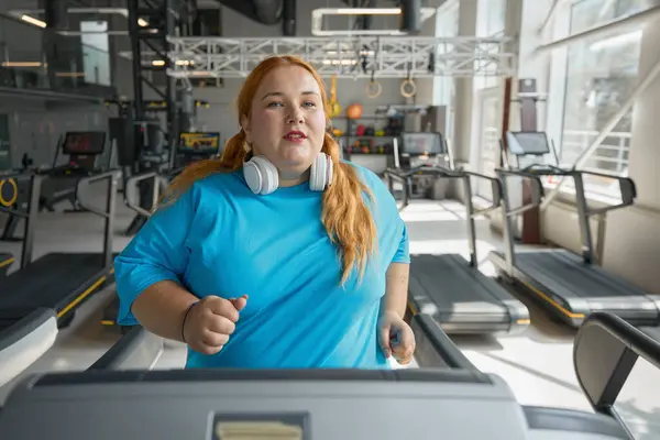 Active obese woman running on treadmill track enjoying cardio exercise for calorie burning. Sportive challenge for slimming