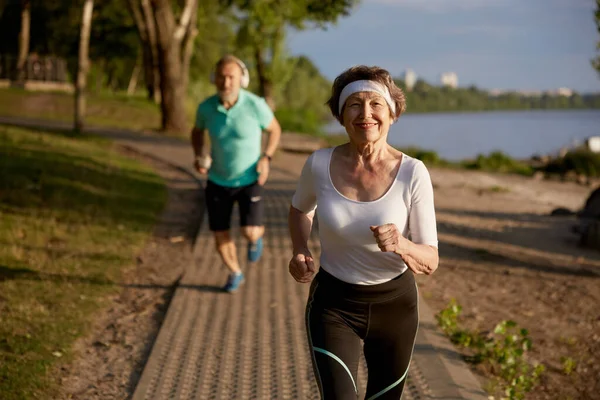 Healthy senior couple running in nature enjoying fresh air and training. Elderly man and woman on retirement doing jogging sports exercise for wellness and wellbeing