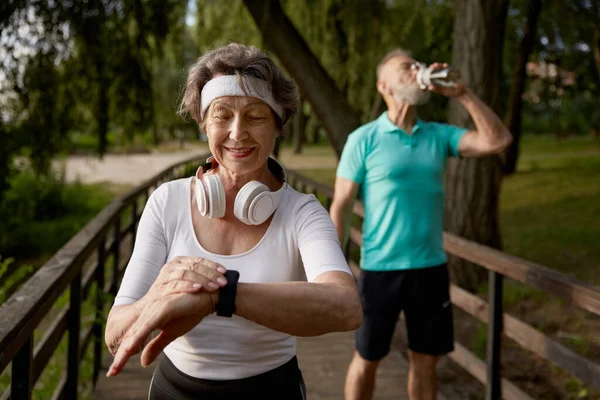Senior fitness woman proud of overtaking her tired husband during morning running workout. Retiree cardio wellness or marathon jog