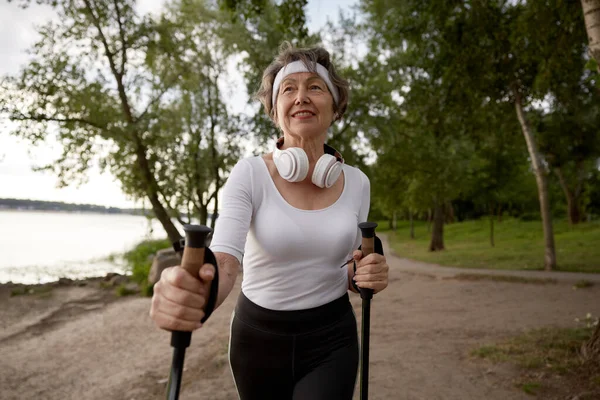 Elderly woman doing sports pole walk enjoying daily physical activity outdoors. Active senior retired sportswoman portrait
