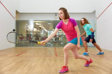 Spor kulübünün iç sahasında squash antrenmanı yapan genç bir çift. Çekici bir kadının raketle topa vurmasına odaklan