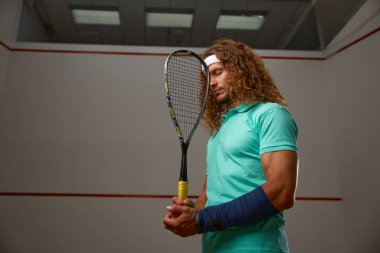 Sırtında raket olan dalgın bir raketbol oyuncusu. Kapalı sahada squash antrenmanı. Profesyonel spor ve hobi konsepti