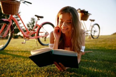 Dışarıda bisiklet gezisi sırasında doğa üzerine kitap okuyan genç bir kadının yakın plan portresi. Dinlenme zamanı, hobi eğlence aktivitesi.