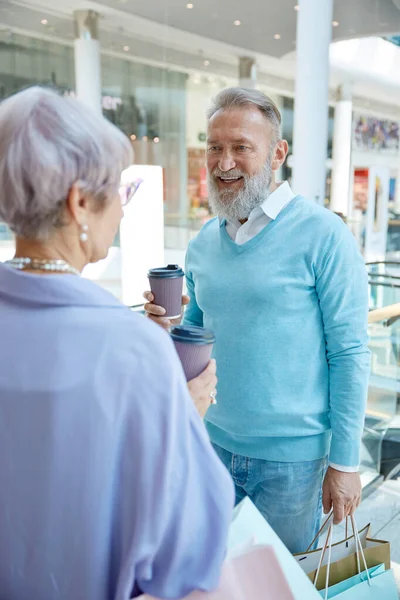 Stylish senior couple drinking coffee taking break during shopping. Happy pensioner enjoying romantic time in shop mall