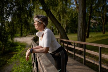 Yeşil şehir parkının harika manzarasının keyfini çıkardıktan sonra gülümseyen yaşlı kadın dinleniyor. Emeklilik konusunda sağlık ve aktif yaşam tarzı kavramı