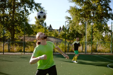 Sporcu dışarıda futbol sahasında arkadaşlarıyla oynarken kafasıyla futbol topuna vuruyor. Atletik erkek grubu antrenmanı favori spor maçının keyfini çıkarıyor