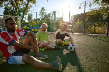Başarılı bir oyun antrenmanından sonra sahada dinlenen gülümseyen futbolcu yüz ifadelerini paylaşıyor. En iyi arkadaşlar spor eğlence zamanı.