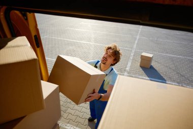 Depo çalışanı elinde kargo kamyonunu boşaltan bir dosya kutusu tutuyor. Envanter yönetimi ve sevkiyat servisi